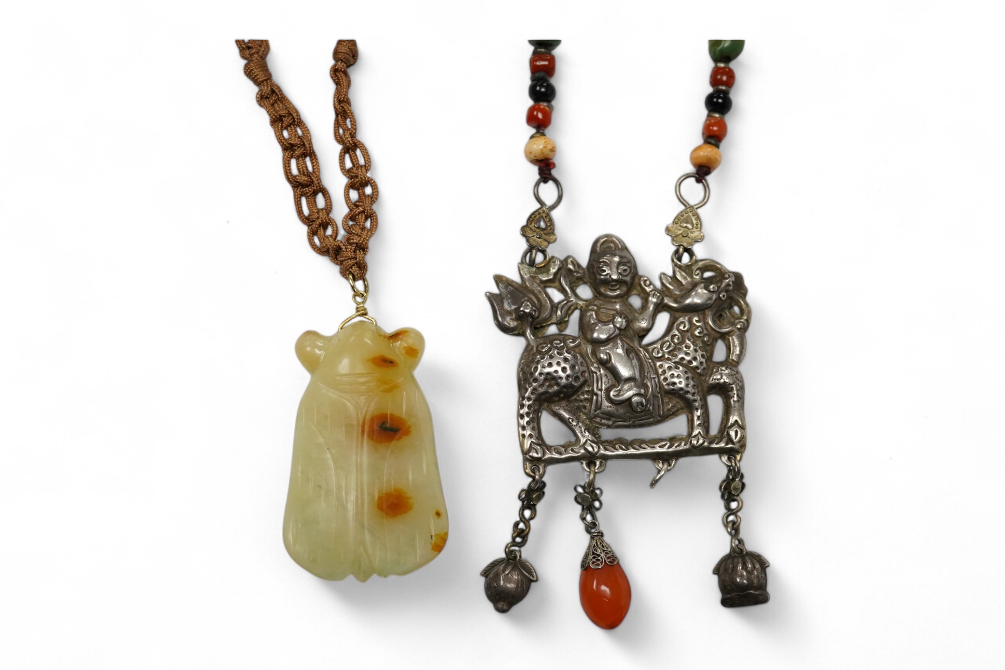 A Chinese celadon and russet jade cicada pendant on cording and a silver and stone mounted chain and pendant of boy riding a qilin, cicada 5.5cm long (2). Condition - tip of cicada wing chipped and on silver pendant one